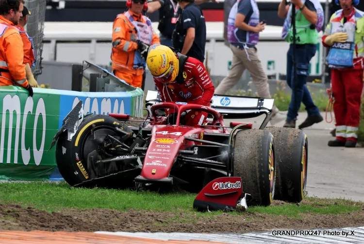 Lewis Hamilton, con casco amarillo y uniforme rojo, saliendo de su Ferrari de Fórmula 1 dañado, con piezas del monoplaza desprendidas sobre el césped.